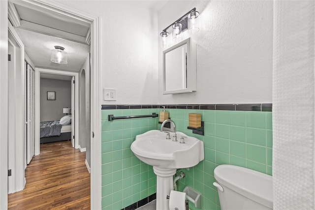 bathroom with wood-type flooring, toilet, tile walls, and a textured ceiling