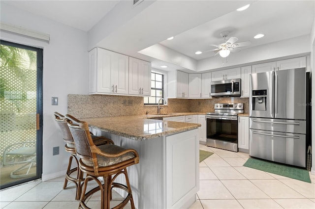 kitchen featuring kitchen peninsula, tasteful backsplash, stainless steel appliances, sink, and white cabinets