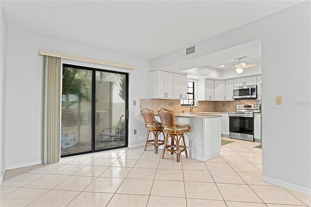 kitchen with a kitchen bar, appliances with stainless steel finishes, kitchen peninsula, light tile patterned floors, and white cabinets