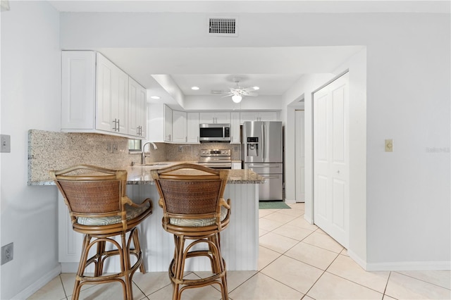 kitchen featuring kitchen peninsula, stainless steel appliances, white cabinetry, and light stone counters