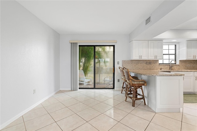 kitchen with white cabinetry, sink, a healthy amount of sunlight, decorative backsplash, and a breakfast bar