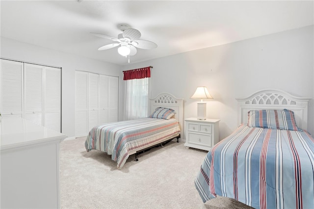 bedroom with ceiling fan, light colored carpet, and multiple closets