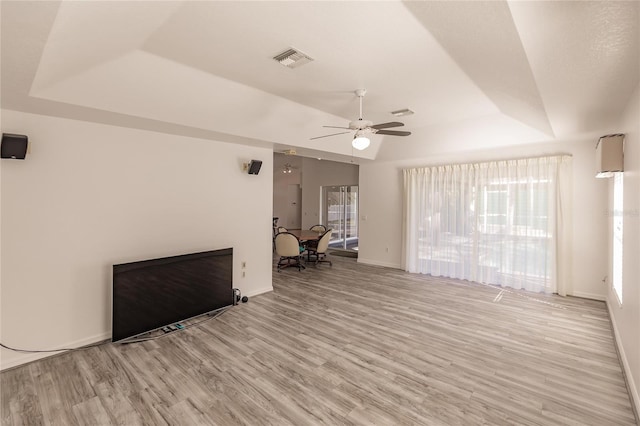 unfurnished living room featuring ceiling fan, light hardwood / wood-style floors, and a tray ceiling