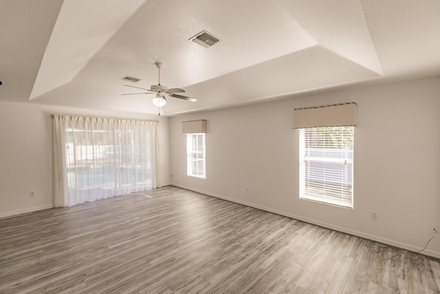 unfurnished room with a raised ceiling, ceiling fan, and a healthy amount of sunlight