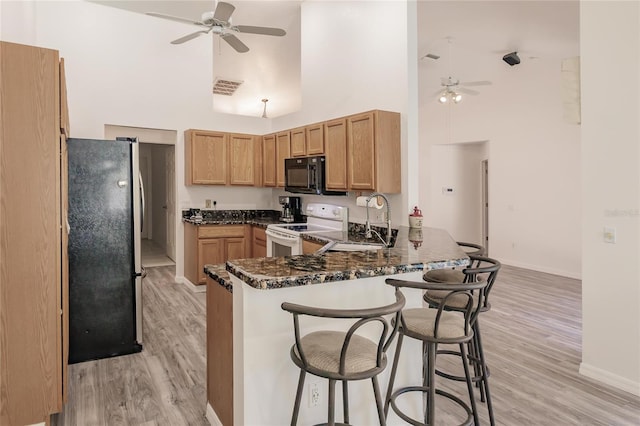 kitchen with kitchen peninsula, a towering ceiling, dark stone counters, white electric range oven, and stainless steel refrigerator