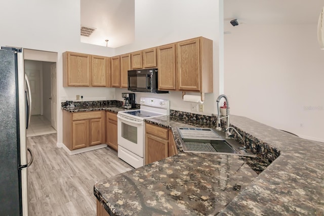 kitchen featuring stainless steel refrigerator, sink, white electric stove, kitchen peninsula, and dark stone counters