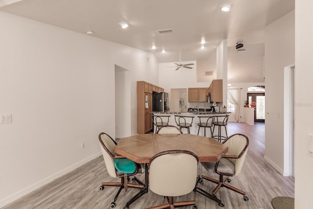 dining area featuring ceiling fan, sink, high vaulted ceiling, and light hardwood / wood-style flooring