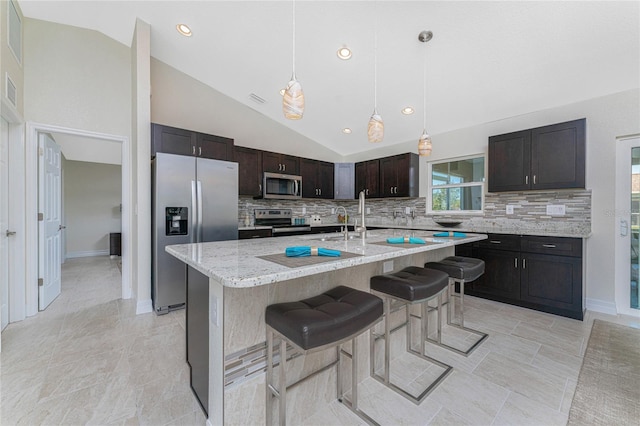 kitchen featuring a kitchen breakfast bar, vaulted ceiling, an island with sink, appliances with stainless steel finishes, and dark brown cabinetry