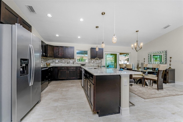 kitchen featuring pendant lighting, sink, stainless steel refrigerator with ice dispenser, an island with sink, and light stone counters