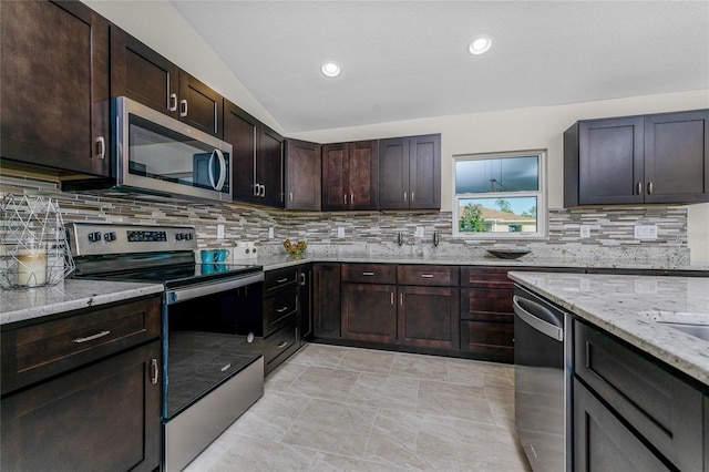 kitchen with dark brown cabinetry, stainless steel appliances, light stone counters, lofted ceiling, and decorative backsplash