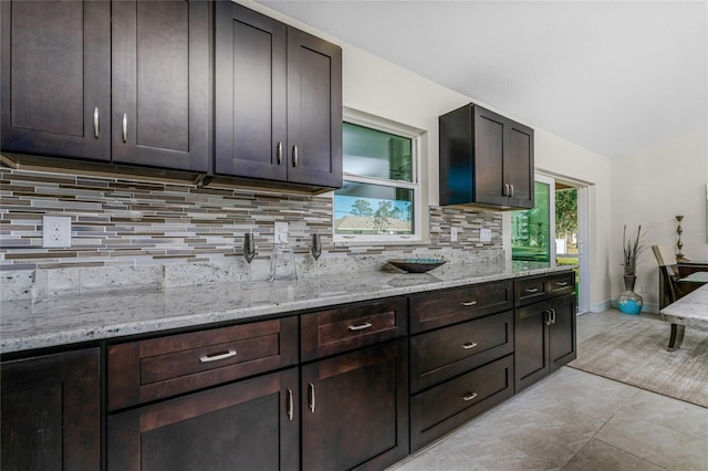 kitchen featuring light stone counters, dark brown cabinetry, light tile patterned floors, and tasteful backsplash