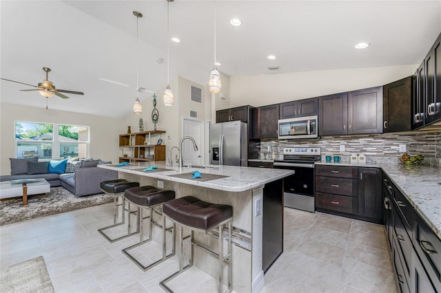 kitchen with appliances with stainless steel finishes, tasteful backsplash, a kitchen island with sink, pendant lighting, and a breakfast bar area