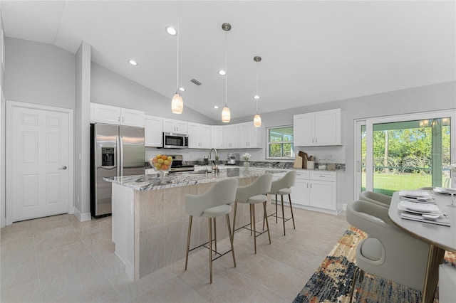 kitchen featuring white cabinets, appliances with stainless steel finishes, backsplash, a kitchen island with sink, and light stone counters