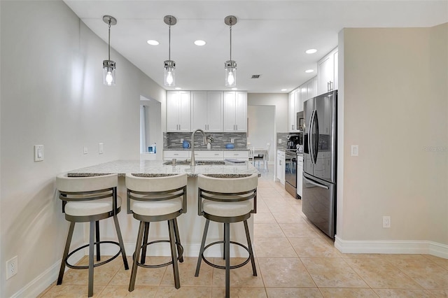 kitchen with pendant lighting, sink, white cabinets, light stone counters, and stainless steel refrigerator with ice dispenser