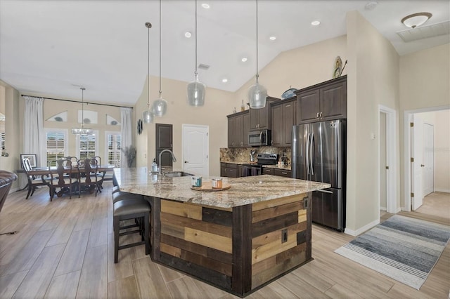 kitchen featuring decorative light fixtures, sink, light stone countertops, a large island with sink, and stainless steel appliances