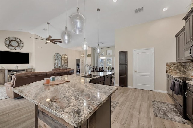 kitchen featuring a large island with sink, decorative light fixtures, stainless steel appliances, sink, and light hardwood / wood-style flooring