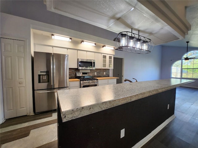 kitchen with tasteful backsplash, stainless steel appliances, pendant lighting, white cabinets, and a kitchen island