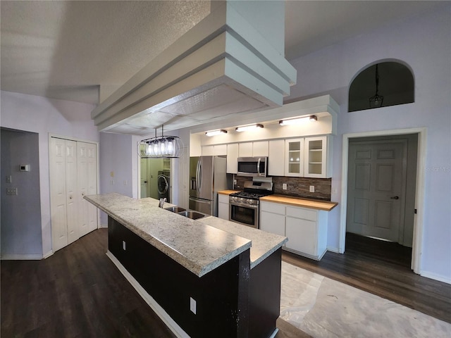 kitchen featuring white cabinetry, tasteful backsplash, an island with sink, decorative light fixtures, and appliances with stainless steel finishes