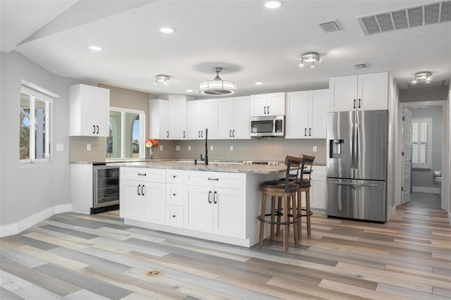 kitchen with a center island, white cabinets, vaulted ceiling, appliances with stainless steel finishes, and beverage cooler