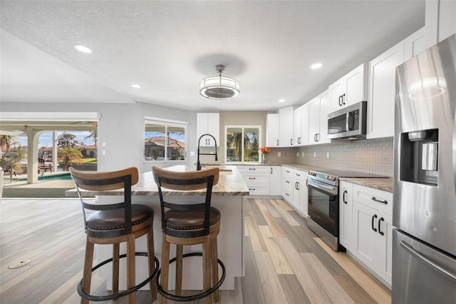 kitchen featuring white cabinets, light stone countertops, appliances with stainless steel finishes, and tasteful backsplash