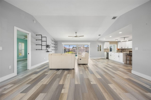 unfurnished living room with sink, lofted ceiling, and light wood-type flooring