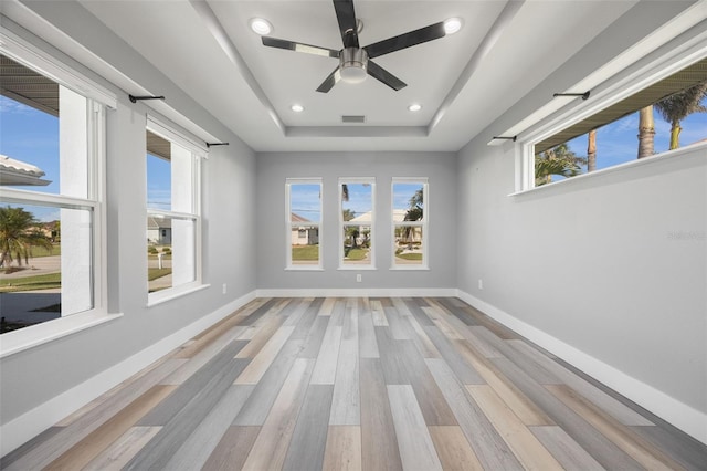 unfurnished room with ceiling fan, a healthy amount of sunlight, light wood-type flooring, and a tray ceiling