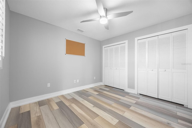 unfurnished bedroom with light wood-type flooring, ceiling fan, and multiple closets