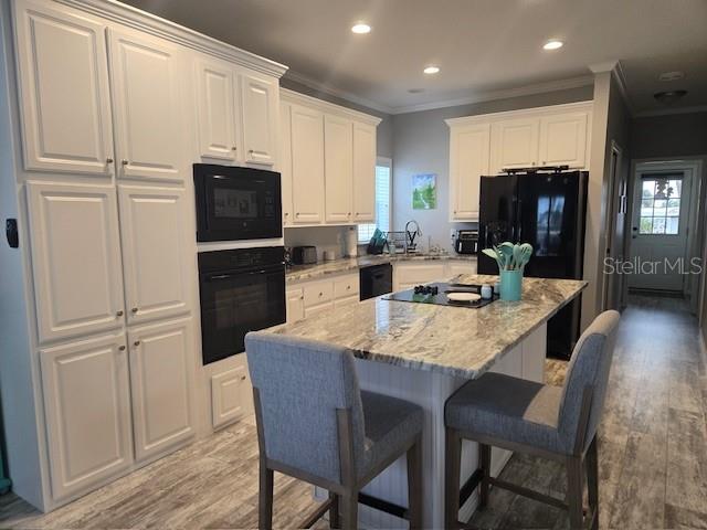 kitchen featuring a kitchen breakfast bar, crown molding, black appliances, white cabinets, and a kitchen island