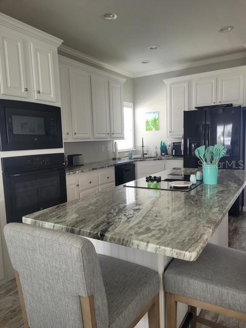 kitchen featuring sink, a kitchen island, a kitchen breakfast bar, white cabinets, and black appliances