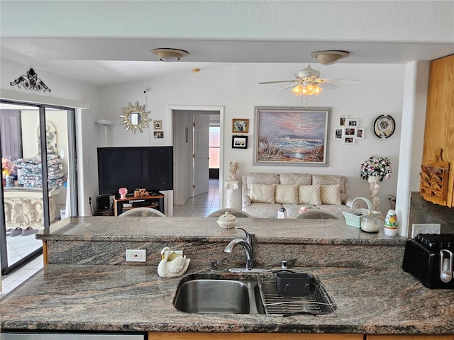 kitchen with ceiling fan, dark stone countertops, light tile patterned floors, and sink