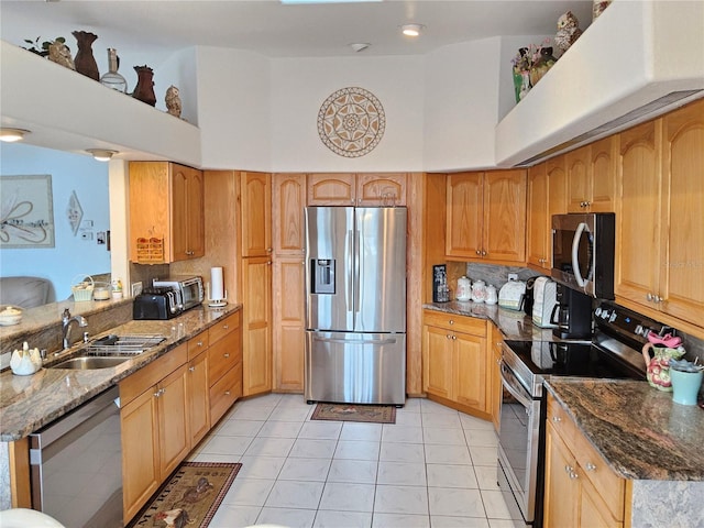 kitchen featuring appliances with stainless steel finishes, sink, light tile patterned floors, dark stone countertops, and a high ceiling