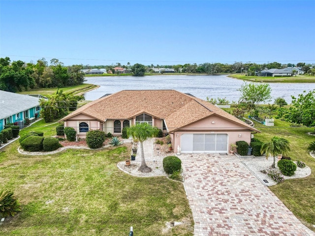 ranch-style home featuring a front lawn, decorative driveway, a water view, and stucco siding