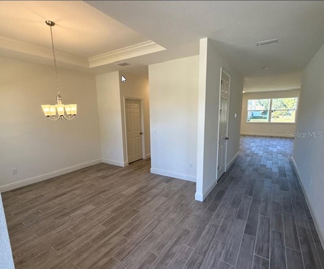 empty room with a tray ceiling, dark hardwood / wood-style floors, and an inviting chandelier