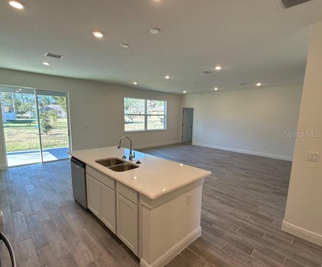 kitchen featuring wood-type flooring, white cabinetry, sink, stainless steel dishwasher, and a center island with sink