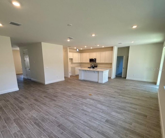 kitchen featuring white cabinets, light wood-type flooring, an island with sink, and sink