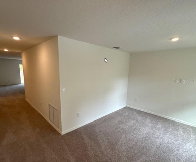 spare room featuring dark carpet and a textured ceiling