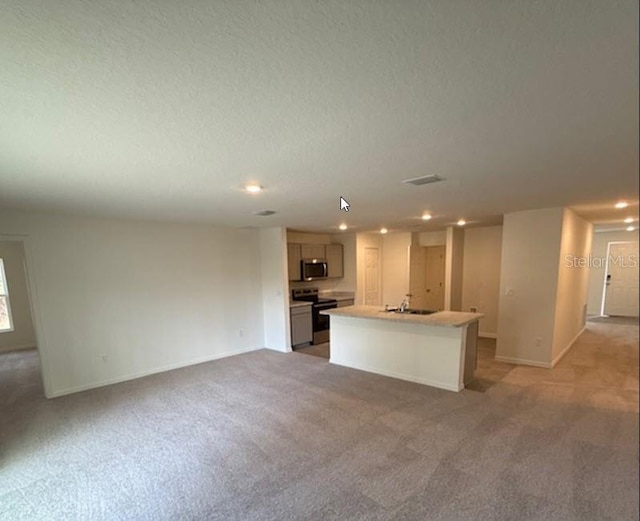 kitchen featuring sink, appliances with stainless steel finishes, a textured ceiling, a center island with sink, and light carpet