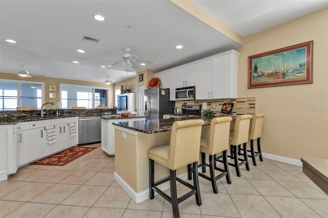 kitchen with white cabinetry, dark stone countertops, kitchen peninsula, a kitchen bar, and appliances with stainless steel finishes