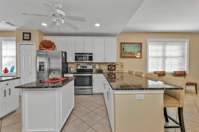 kitchen featuring a center island, white cabinets, decorative backsplash, appliances with stainless steel finishes, and light tile patterned flooring