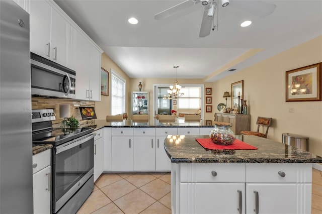 kitchen with white cabinetry, stainless steel appliances, kitchen peninsula, light tile patterned floors, and ceiling fan with notable chandelier