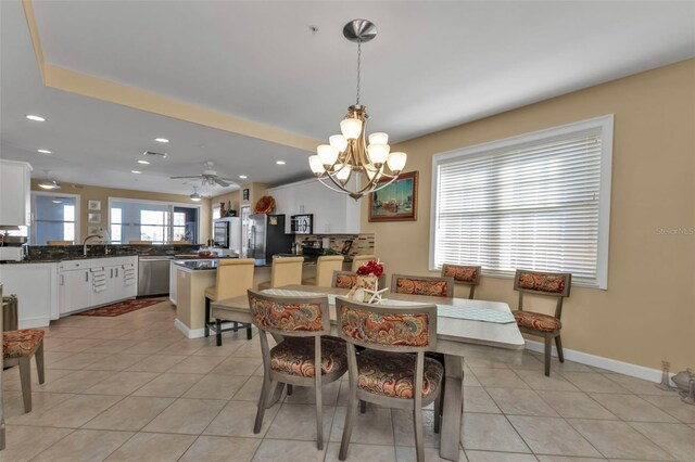 dining area featuring sink, light tile patterned floors, and ceiling fan with notable chandelier