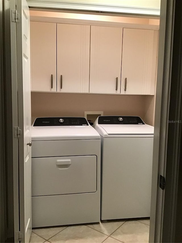 clothes washing area featuring washing machine and clothes dryer, light tile patterned flooring, and cabinets