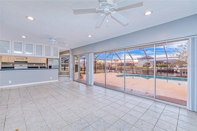 unfurnished living room with ceiling fan, sink, light tile patterned floors, a textured ceiling, and a water view