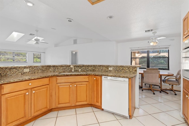 kitchen with lofted ceiling with skylight, white dishwasher, sink, light tile patterned floors, and stone countertops