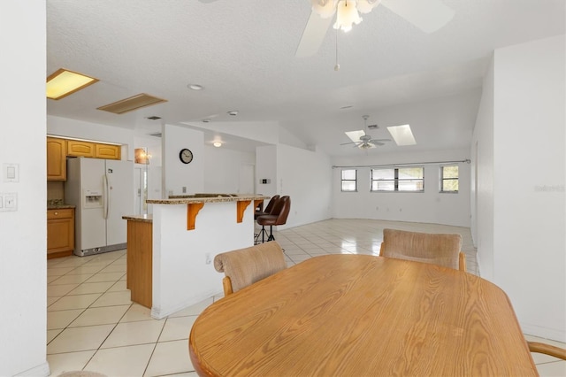 unfurnished dining area with lofted ceiling with skylight, light tile patterned flooring, and ceiling fan