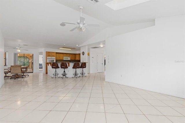 tiled living room featuring lofted ceiling with skylight and ceiling fan