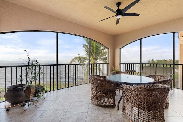 sunroom featuring ceiling fan and a water view