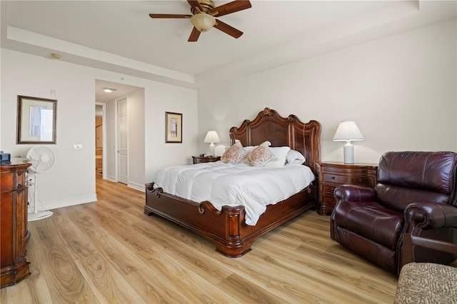 bedroom featuring a tray ceiling, ceiling fan, and light wood-type flooring