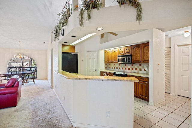 kitchen with stainless steel appliances, light carpet, kitchen peninsula, decorative backsplash, and ceiling fan with notable chandelier