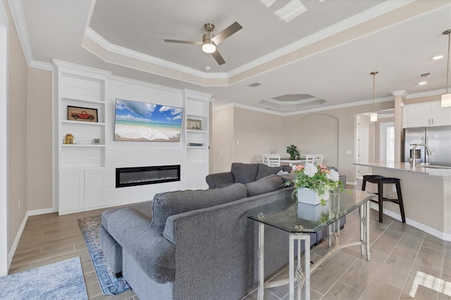 living room featuring ceiling fan, crown molding, a fireplace, and a tray ceiling